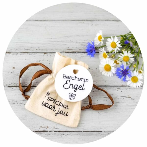Bescherm Engel pocket hug liggend op een draagtasje met enkele wilde bloemen vlakbij