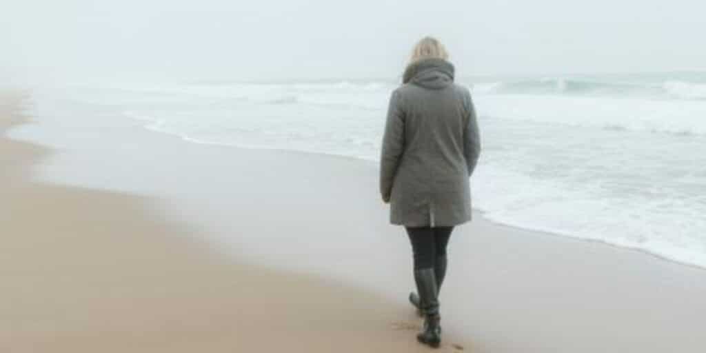Als het stof is gaan liggen. Vrouw loopt alleen langs de branding op een winters strand