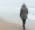 Als het stof is gaan liggen. Vrouw loopt alleen langs de branding op een winters strand