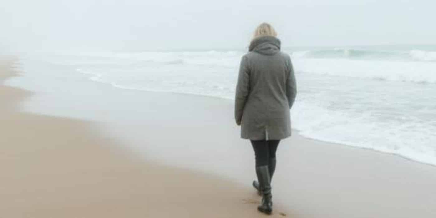 Als het stof is gaan liggen. Vrouw loopt alleen langs de branding op een winters strand